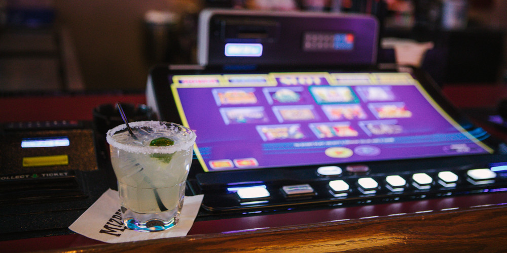 A cocktail sitting next to a bartop slot machine.